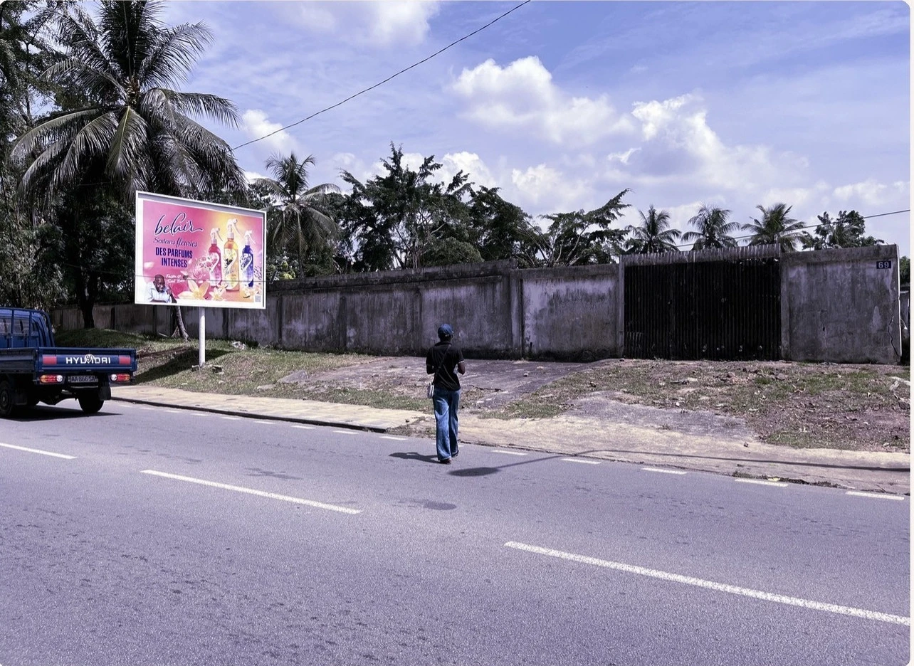 Original Abidjan field-collection photograph showing a collector near an outdoor advertising face